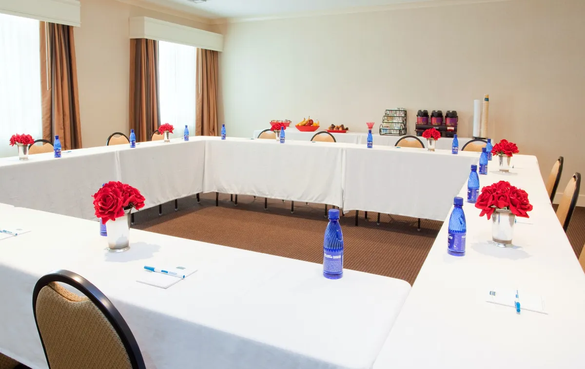 A thoughtfully arranged event or meeting space with neat tables, fresh red flowers, water bottles, and a well-presented snack selection. The setup encourages collaboration, making it ideal for business meetings, workshops, or group gatherings.
