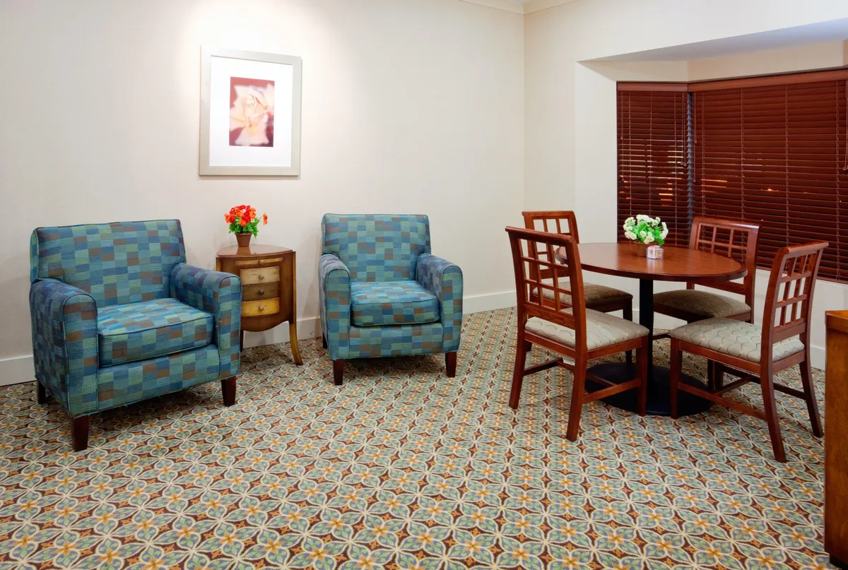 This image displays a cozy dining area featuring a round table surrounded by blue patterned chairs, a decorative flower arrangement as the centerpiece, and framed artwork on the wall. The setting is inviting and ideal for both family gatherings and intimate meals, creating a welcoming ambiance.
