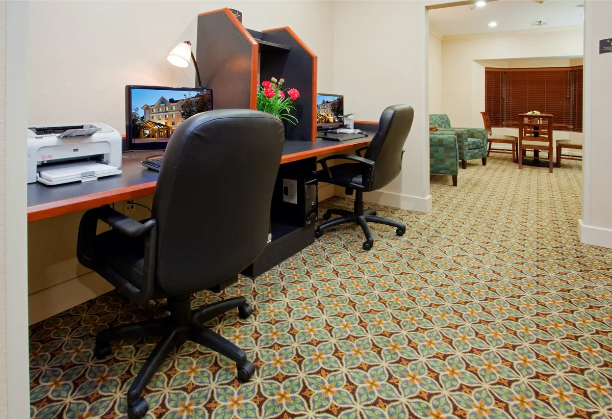 A productive workspace setup is featured here, with computers, a printer, a spacious desk, and a comfortable seating area. Decorative touches, such as a flower arrangement, soften the look, blending functionality with a welcoming environment ideal for catching up on work or planning activities.