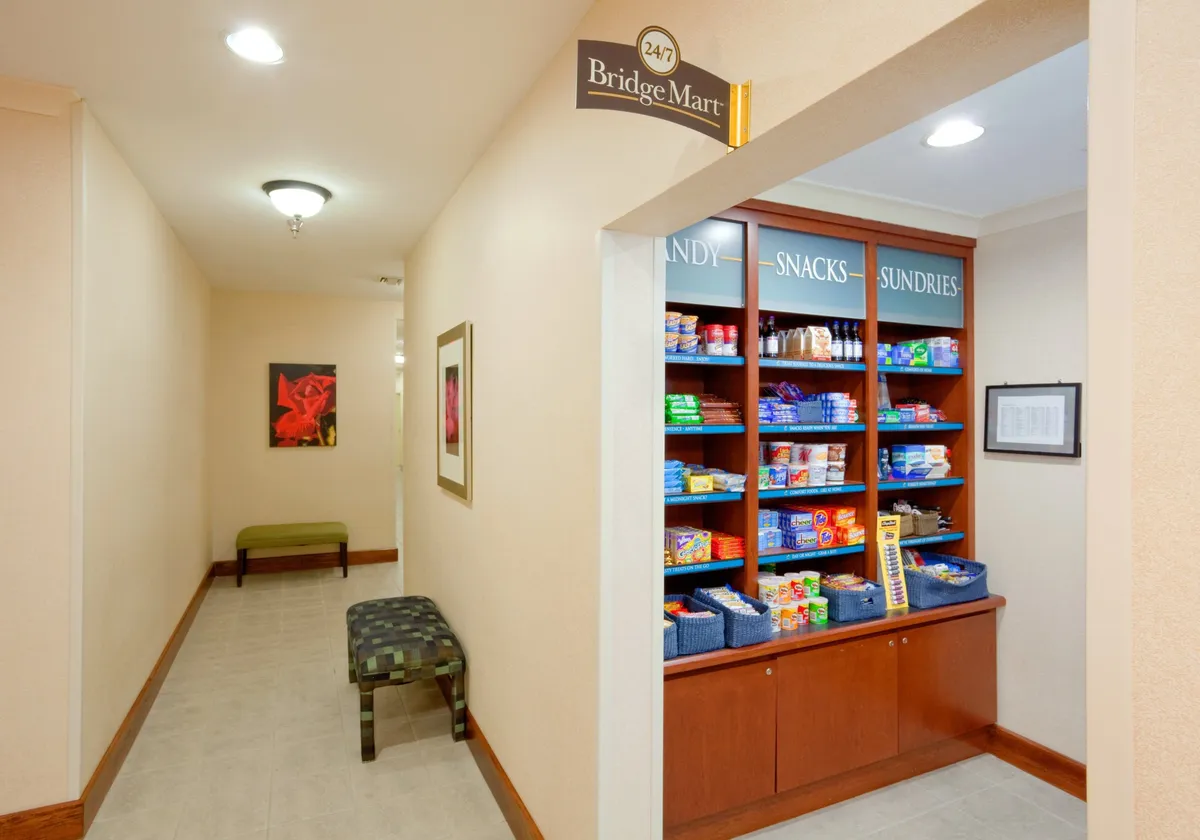 The image depicts a welcoming interior space featuring a snack display, bench seating, and inviting artwork. The area is designed for guests to relax, grab refreshments, and socialize, conveying a convenient and community-oriented atmosphere.